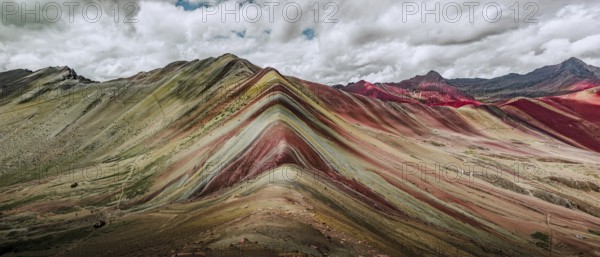 A stunning panoramic capture of Vinicunca, or Rainbow Mountain, famous in Peru for its colorful, layered mineral deposits, under a dramatic sky