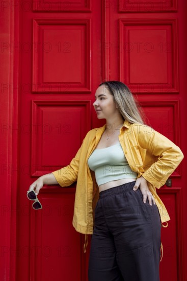 A fashionable woman in a vibrant yellow shirt stands confidently against a bright red door on a city street, embodying the essence of urban exploration and travel