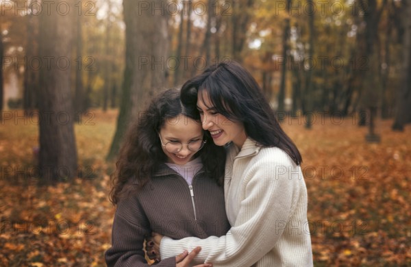 A mother and daughter share a warm embrace surrounded by autumn leaves in a forest. The cozy moment captures the essence of family bonds during the fall season