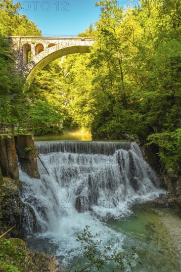 Stunning waterfall cascading beneath a stone bridge in the picturesque vintgar gorge near bled, slovenia, creating a breathtaking natural spectacle