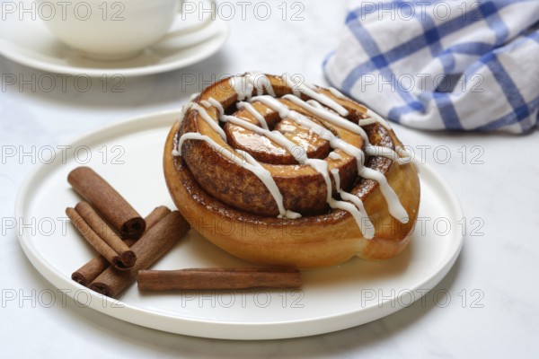Cinnamon roll on plate and cinnamon sticks