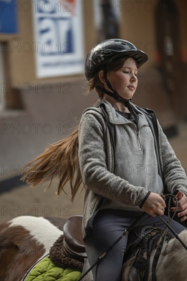 Little girl, 10 years old, in the saddle on a horse in an indoor riding arena, Mecklenburg-Vorpommern, Germany