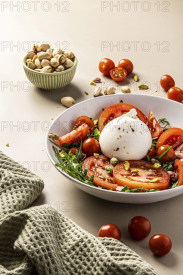 A vibrant salad featuring creamy burrata, juicy tomatoes, and crunchy pistachios. Served in a white bowl with a fresh texture, perfect for a nutritious meal experience