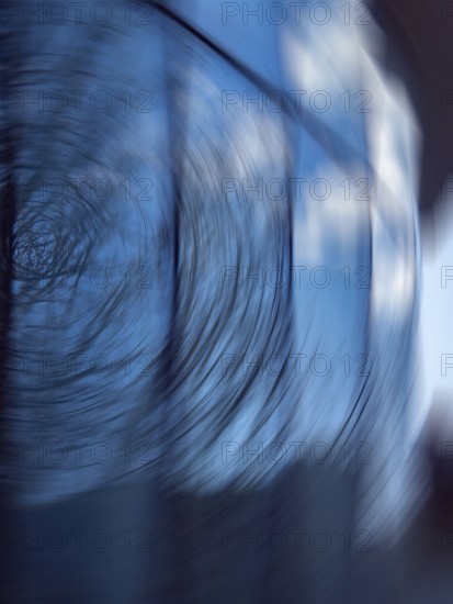 A captivating abstract photograph featuring a swirling motion blur against a blue background. The image includes subtle reflections on glass, creating an intriguing visual effect