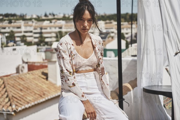 A stylish woman enjoys a sunny day on a rooftop, wearing trendy summer fashion The urban backdrop enhances the relaxed and chic vibe of her lifestyle choice
