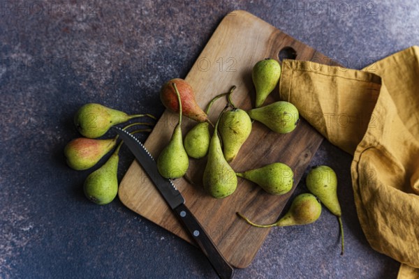 A collection of wild pears is artfully arranged on a rustic wooden cutting board. The setting creates a natural, fresh, and inviting atmosphere, highlighted by a soft yellow cloth