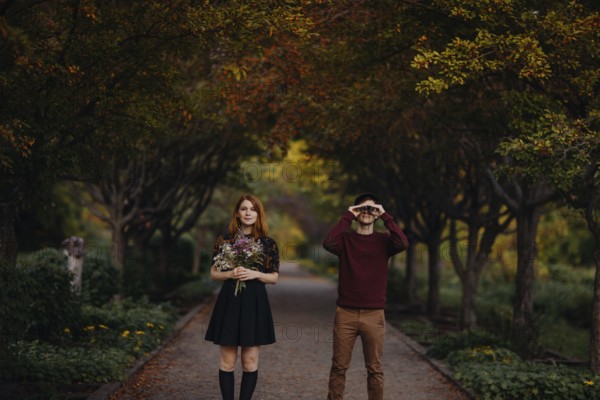 A couple enjoying a beautiful fall day in Quebec, Canada. The woman holds a bouquet of wildflowers, while the man looks through binoculars, surrounded by autumn foliage