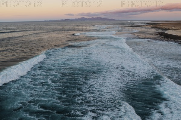 A serene view of Popcorn Beach as twilight settles, showcasing gentle waves rolling onto the textured shoreline under a pastel sky