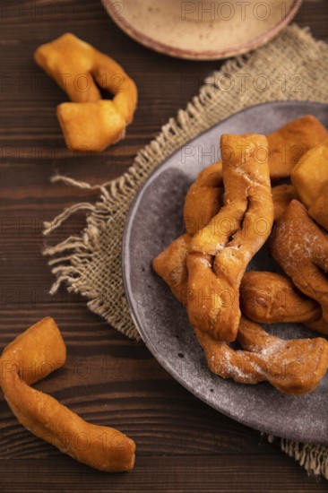 Crunchy biscuit Brushwood cookies sprinkled with powdered sugar on brown wooden background and linen textile, cup of coffee, side view, close up, selective focus