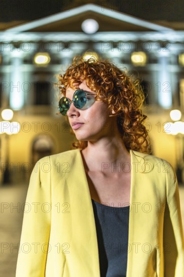 Vertical photo of a distracted modern woman in sunglasses and yellow jacket in the city at night