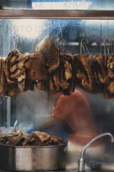 Unrecognizable person preparing traditional street food in Hong Kong, with hanging dried items and steam rising from a cooking pot