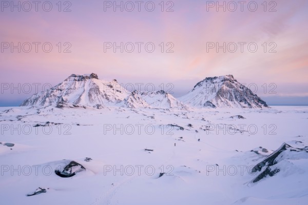 A breathtaking view of Katla Glacier's rugged snow-covered mountains beneath a pastel pink sunrise sky. The untouched snowy plain below adds a sense of serenity and vastness to the arctic scene