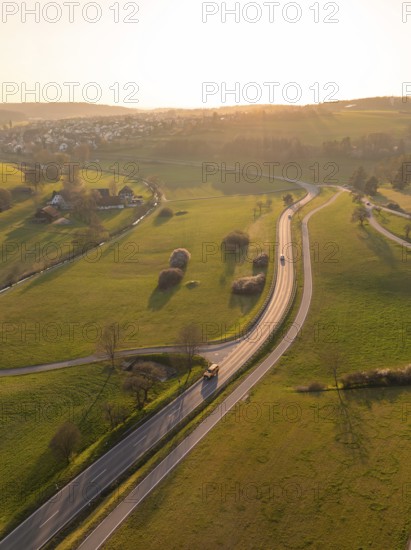 Winding country road through green fields and trees, under a warm sunset sky, Gechingen, district of Calw, Black Forest, Germany