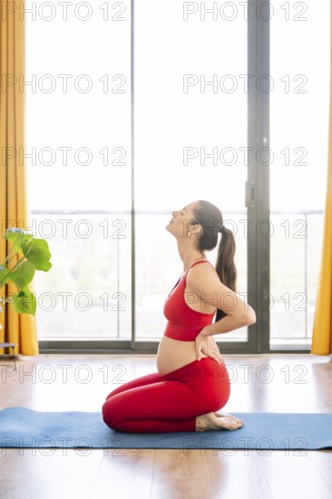 A pregnant woman practices yoga in a serene setting, embracing wellness and relaxation. She kneels on a yoga mat in comfortable activewear, promoting calm and health