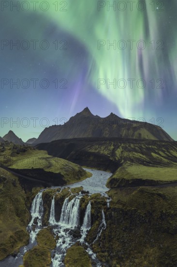 Breathtaking view of the Aurora Borealis cascading over a serene Icelandic waterfall surrounded by rugged mountains under a starry sky