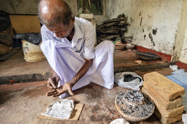 A man is busy with coal and a newspaper clipping in a quiet workshop, a man is burning sapphires in a small oven in the town of Ratnapura in Sri Lanka
