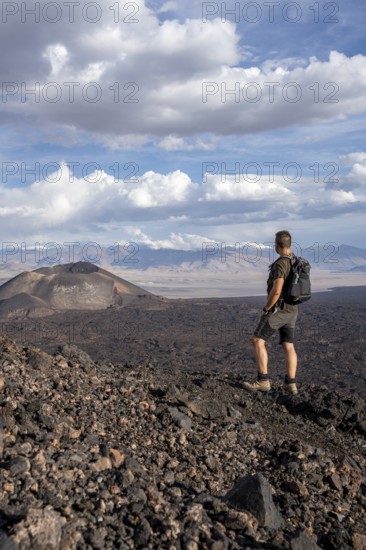 Hiker looks at a vast volcanic landscape under a cloudy sky, Argentina, volcanoes, lava field, Antofagasta
