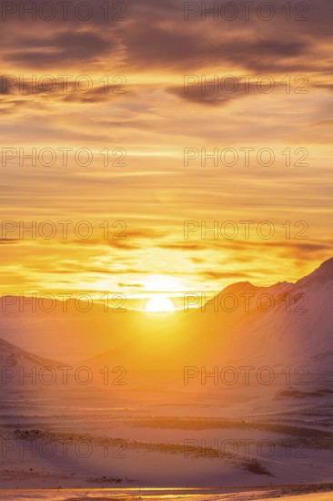 A breathtaking view of a vibrant winter sunset illuminating snow-covered mountains in Iceland. The warm colors contrast the icy landscape, creating an awe-inspiring scene