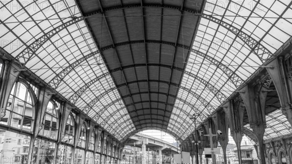 Black and white photo of the grand interior of a historic railway station in Nice, France, featuring stunning arched metal frameworks and intricate details