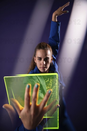 A young woman engages with a neon green futuristic device, highlighting modern technological innovations and concepts, set against a vibrant purple backdrop