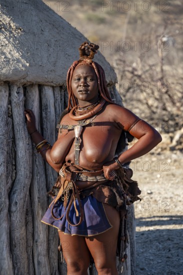 Married Himba woman leaning against a traditional mud house, traditional Himba village, Kaokoveld, Kunene, Namibia