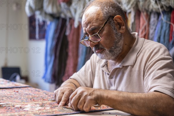 A senior Iranian master skillfully restores a traditional carpet in his well-equipped workshop in Salzburg, Austria, focusing intently on his rare craft