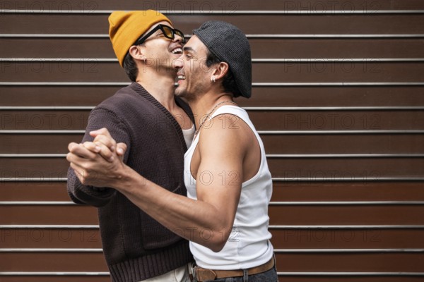 A joyful couple dances and smiles, capturing a moment of happiness and love. They wear casual outfits, with a playful orange hat and embrace warmly against a striped background