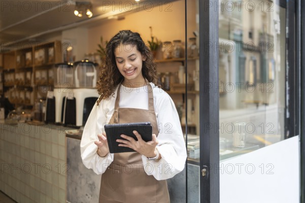 A smiling clerk wearing an apron uses a tablet to manage inventory at an organic bulk store. Shelves stocked with jars provide a rustic backdrop, creating a warm, inviting atmosphere