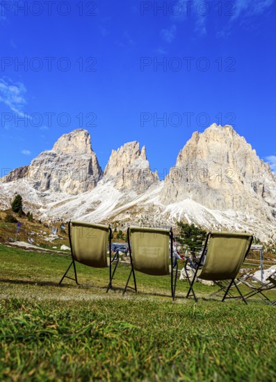 Three camping chairs in a meadow at Passo Sella in front of dramatic mountain peaks under a clear sky