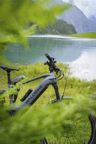 An e-bike is parked on the lakeshore. The surrounding nature is lush and green, and the mountains can be seen in the background: Stilluptal, Zillertal. Austria