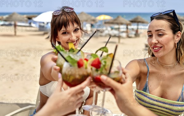 Friends gather on a sunny beach, enjoying colorful cocktails while celebrating summer. Laughter and joy fill the air as they toast with drinks in hand