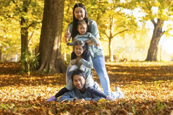 Asian family having fun in an autumn park, with laughter and playful energy. Children enjoying time outdoors, surrounded by fallen leaves and bright sunlight, capturing joy together
