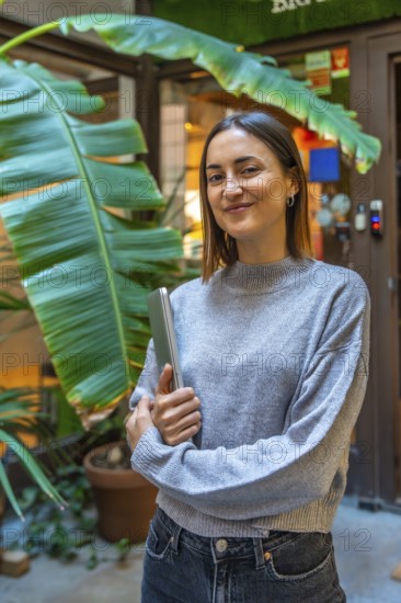 Vertical portrait of a beauty young female entrepreneur standing outside a coworking office holding a laptop