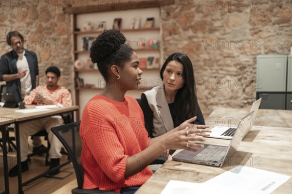 A diverse group of professionals engages in discussion within a modern coworking space, highlighting teamwork, creativity, and informal yet productive work environments