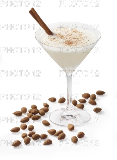 Cocktail in a martini glass in front of a white background, a cinnamon stick and cinnamon powder as garnish, almonds as base decoration, studio shot