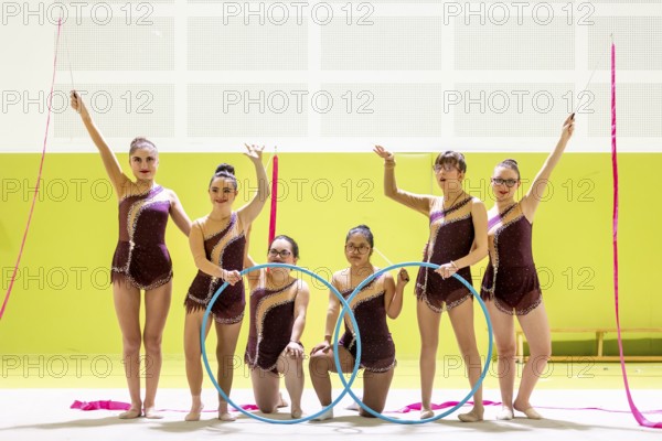 Group of gymnasts whit disability in maroon outfits performing with hoops and ribbons in a brightly lit arena. They showcase elegance, and athleticism, creating a captivating display and inclusive