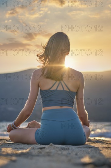 A woman sits in Padmasana on the beach, practicing Chin mudra meditation as the sun sets behind her