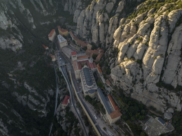 An aerial view of the Montserrat Abbey in Catalonia, Spain, showcases its unique placement amidst rugged mountains, highlighting its architectural beauty and natural surroundings