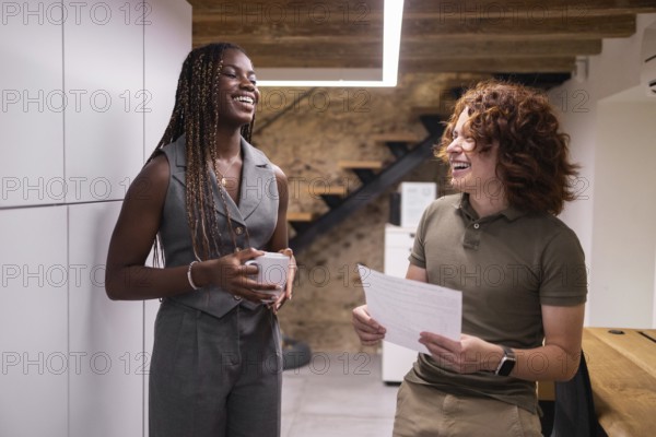 Two coworkers enjoy a lighthearted conversation in a modern office setting, fostering a positive and collaborative work environment with a seemingly relaxed atmosphere