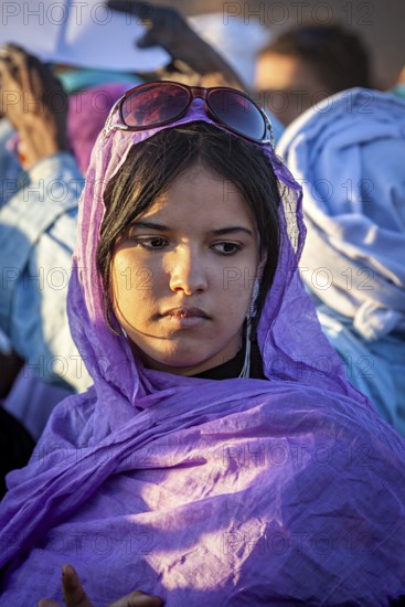 A pensive woman in a purple robe and sunglasses in the evening light, Veiled woman at the Tamanrasett Festival in the Sahara in Algeria
