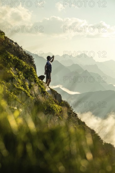 A man takes a break from trail running to hydrate, standing on a scenic mountain path with distant peaks in view. The pause showcases endurance and nature appreciation