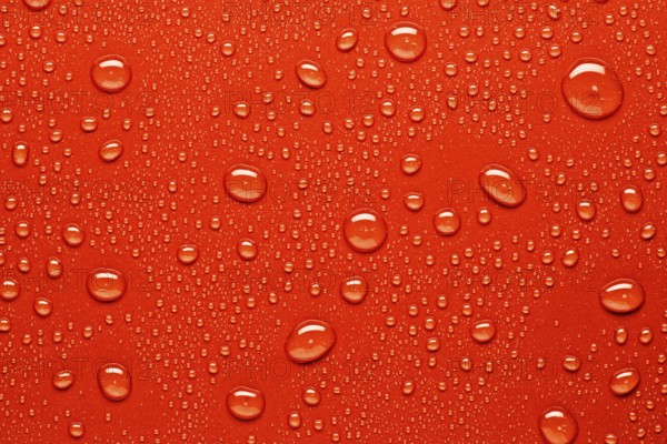 Close up of water droplets on a bright red surface, capturing the texture and varying sizes of the droplets. Ideal for backgrounds, design projects, or abstract art