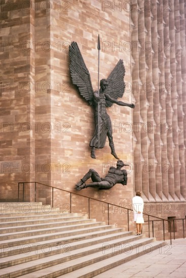 Standing woman with view of the sculpture Coventry Cathedral Church, West Midlands, England, United Kingdom, March 1966 St Michael's Victory over the Devil 1958 Bronze sculpture by Jacob Epstein