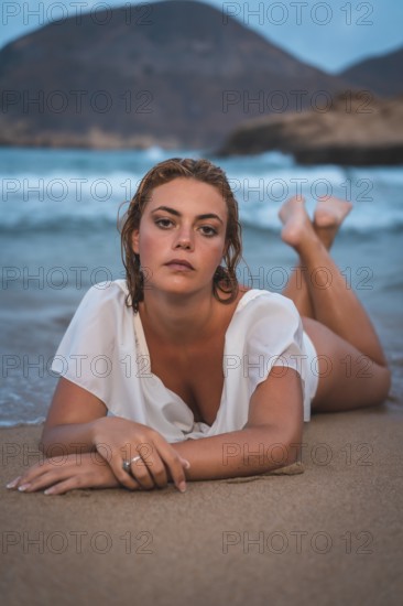 Lifestyle of a blonde Caucasian girl in a white swimsuit. Lying on the sand after getting out of the water with the sea in the background
