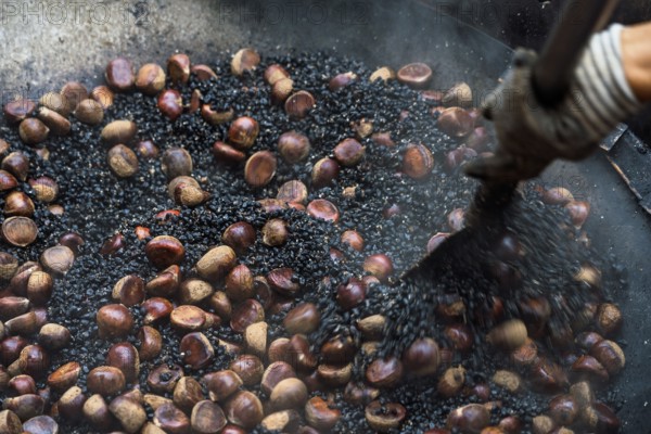 Close-up view of a cropped unrecognizable person roasting fresh chestnuts in a large pan at a Hong Kong street market, showcasing the traditional method of snack preparation