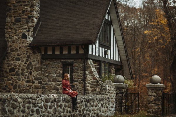 A woman sits by a rustic stone cottage in the Quebec countryside, surrounded by the warm colors of autumn. The scene captures the essence of peaceful rural living