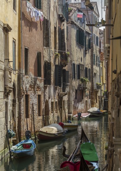 Narrow canal between tall old buildings, lined with boats in a quiet, historic neighbourhood, Venice, Italy