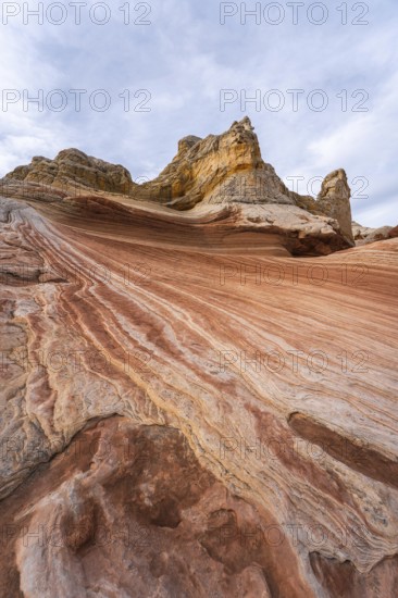 Striking landscape showcasing the vibrant, swirling rock formations of White Pocket in Arizona, USA, with dynamic layers of red and orange sandstone against a cloudy sky