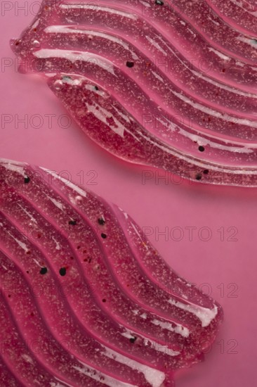 A detailed view of pink scrub and cosmetic gel, elegantly smeared on a pink surface, showcasing the texture and elements within the product