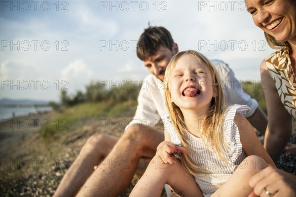 A joyful family enjoys a sunny day on a picturesque Italian beach. The playful child is the center of attention, capturing the essence of happiness and family bonding